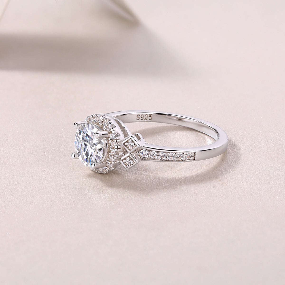 Silver round moissanite ring with geometric shoulder accents on a light blue background.