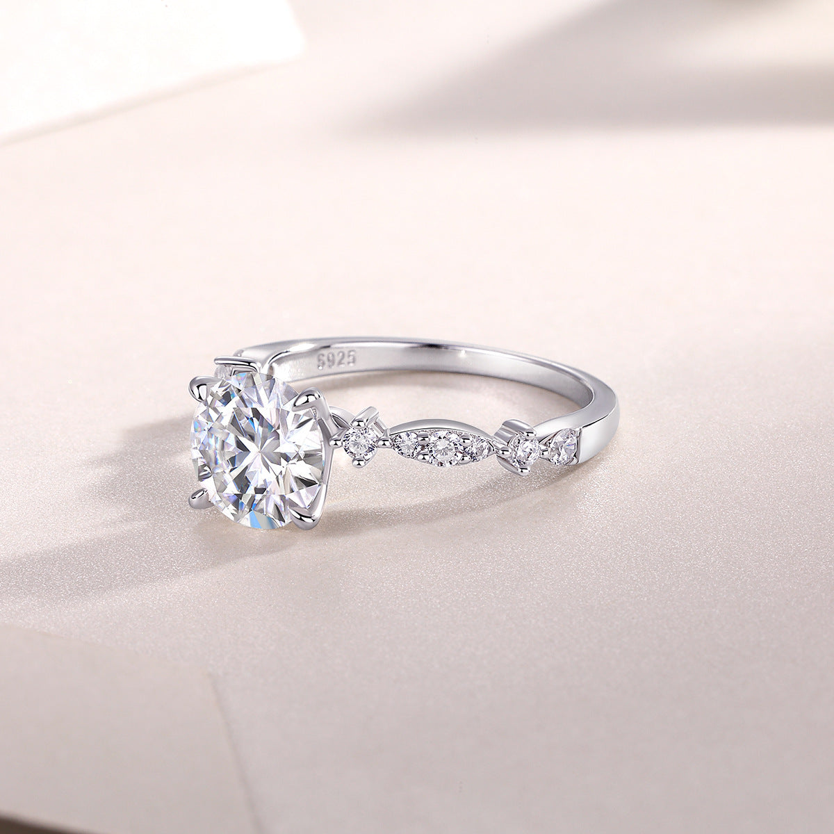 Round cut moissanite leaf station ring resting on light surface.