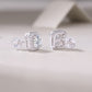 Pair of round cut moissanite octagon cushion halo stud earrings resting on textured surface.
