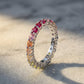 Silver round rainbow gradient moissanite eternity band ring standing on travertine surface