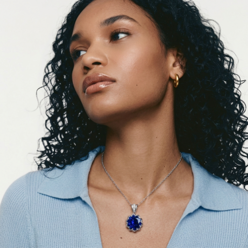 Woman wearing a blue gemstone necklace and gold earring against a neutral background