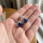 Blue gemstone earrings held in a hand with a blurred background