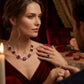 Moody lifestyle portrait of a model in a red velvet dress wearing a royal crimson ruby choker necklace at a candlelit gala dinner.