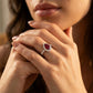 Close-up editorial portrait of a model displaying a royal pigeon-blood ruby teardrop halo ring under warm professional studio lighting.