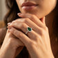Close-up editorial portrait of a model displaying a royal vivid green emerald teardrop halo ring on her finger.