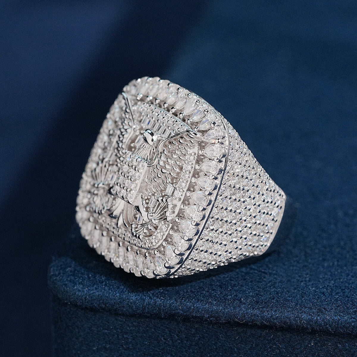 Side profile view of S925 silver iced out moissanite eagle cushion ring on dark blue background