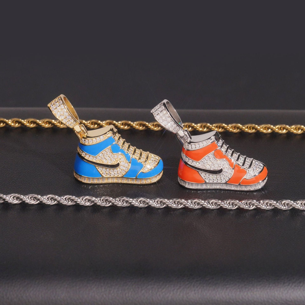 Enamel sneaker moissanite pendants in orange and blue displayed with silver and gold rope chains   