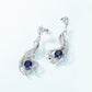 Artistic close-up of 5ct blue sapphire wave earrings on clean background.