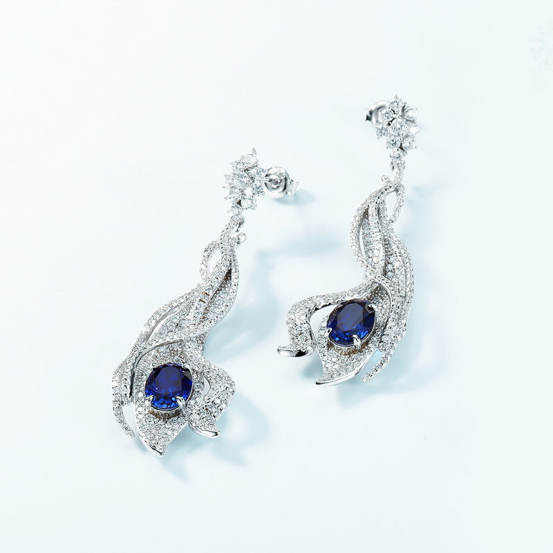 Artistic close-up of 5ct blue sapphire wave earrings on clean background.