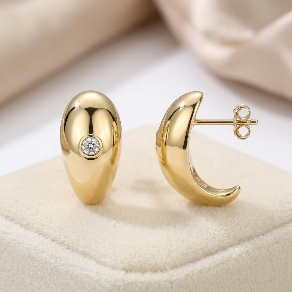 High polish gold sculptural teardrop stud earrings with embedded moissanite resting on a display pad.