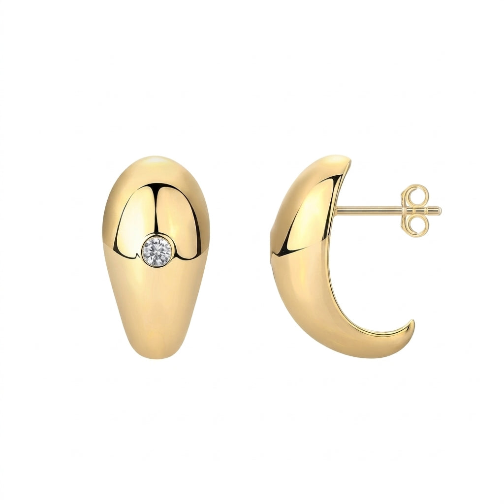 Pair of gold sculptural teardrop earrings with bezel set round moissanite on white background.