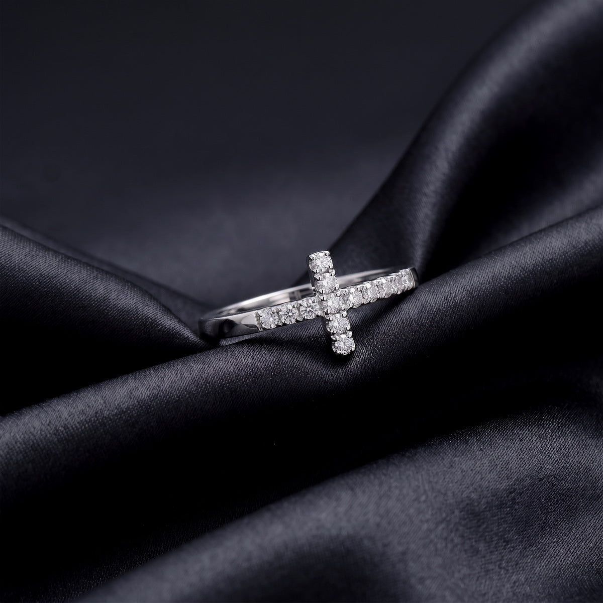 Horizontal sideways cross lab grown diamond ring resting flat on dark black silk fabric