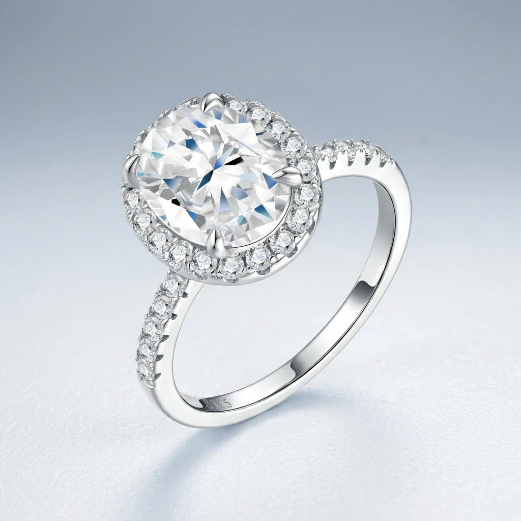 Silver oval moissanite ring with pave halo resting on a soft blue gradient background.