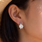 Model wearing six-prong round diamond solitaire huggie hoop earrings under sunlight.