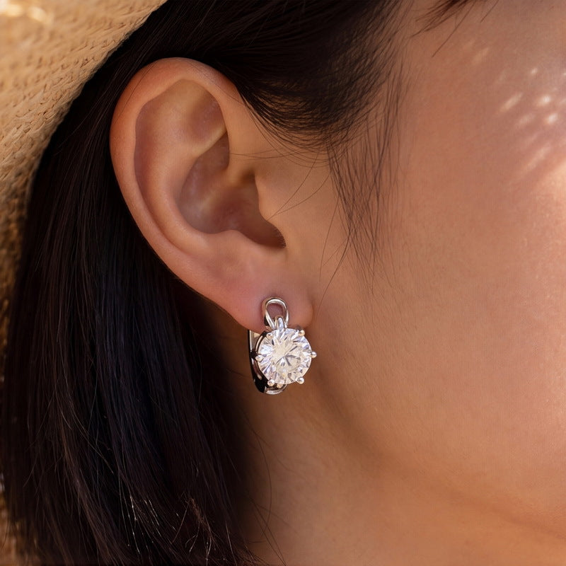 Model wearing six-prong round diamond solitaire huggie hoop earrings under sunlight.