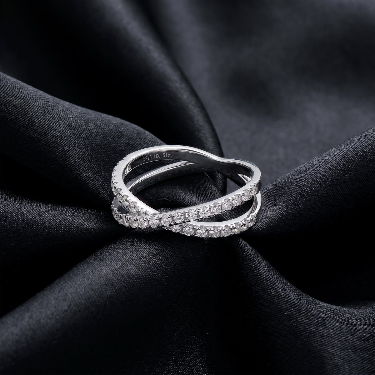 Sparkling lab grown diamond criss cross band ring resting flat on dark black silk fabric