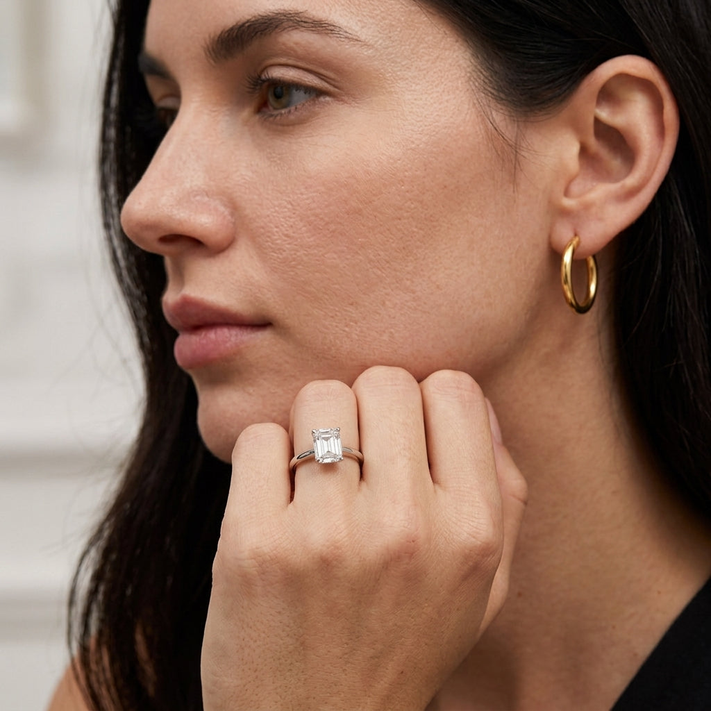 Model wearing square emerald cut solitaire engagement ring near chin.