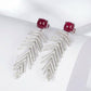 High-angle perspective view of a pair of handcrafted lab-grown ruby wheat chandelier earrings with crisp shadows.