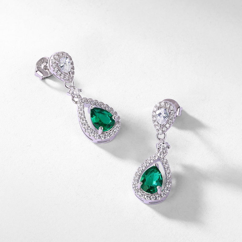 Diagonal overhead studio shot of statement emerald teardrop pave fringe earrings casting a soft gradient shadow.