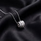 Angled view of three ring princess and round cut lab grown diamond barrel pendant necklace resting on dark black silk