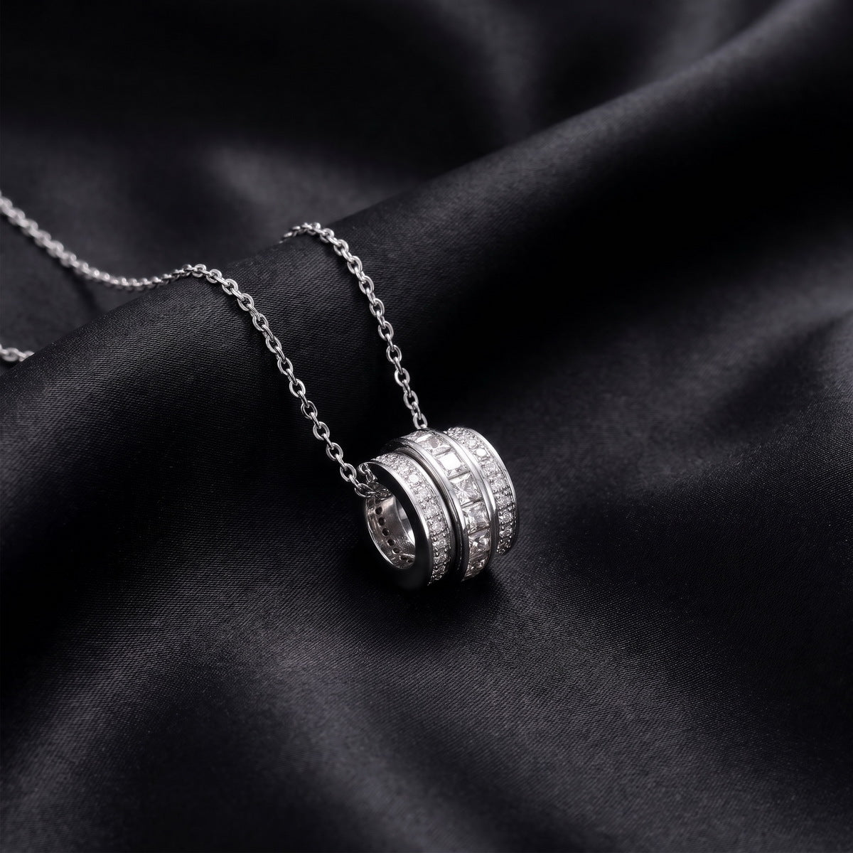 Angled view of three ring princess and round cut lab grown diamond barrel pendant necklace resting on dark black silk