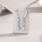Graduated bezel set moissanite linear drop earrings displayed on grey paper card.