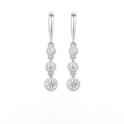 Three stone moissanite drop earrings with graduated bezel set linear dangle on white background.
