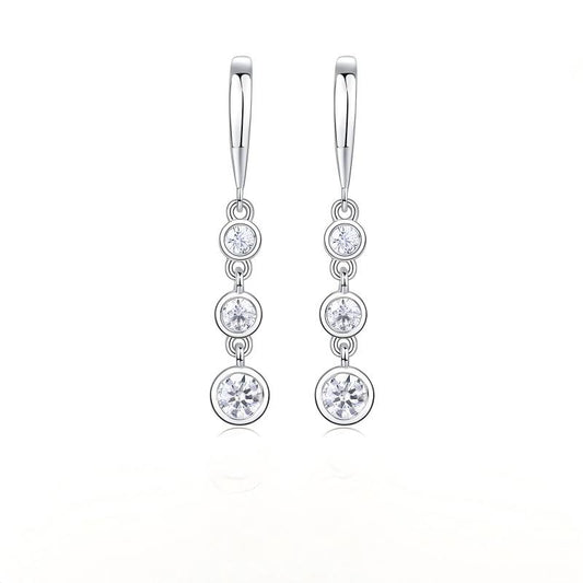 Three stone moissanite drop earrings with graduated bezel set linear dangle on white background.