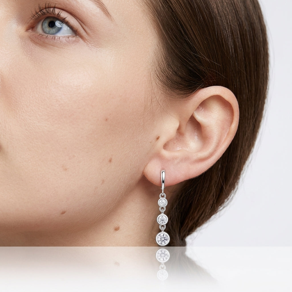 Close-up view of model wearing three stone graduated bezel moissanite dangle earrings.