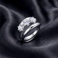Round three-stone engagement ring with matching curved guard band on dark silk.