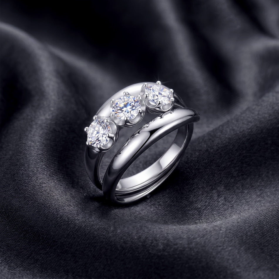 Round three-stone engagement ring with matching curved guard band on dark silk.
