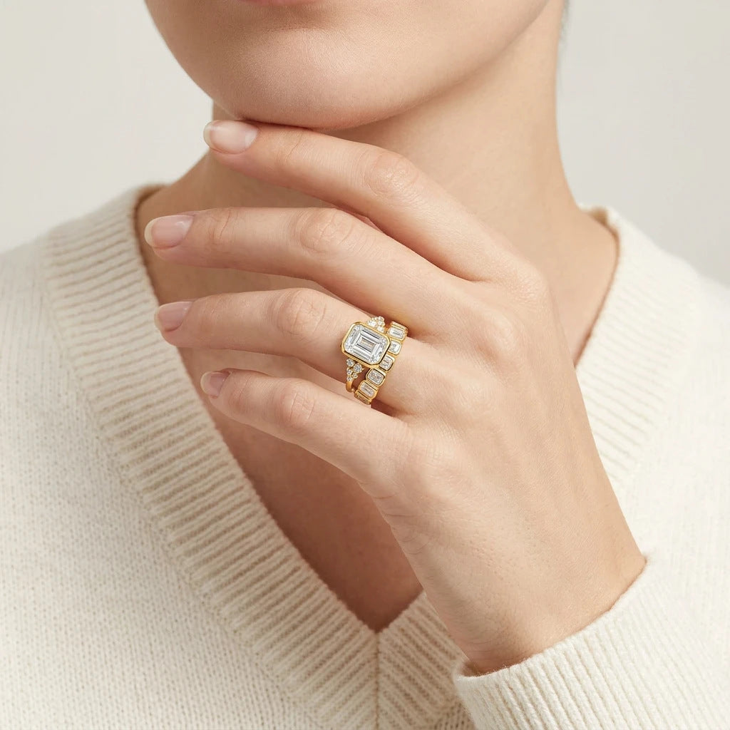 Editorial fashion lookbook portrait of a model styling a gold bezel set emerald cut moissanite bridal ring set across her cardigan.