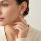 Editorial fashion lookbook portrait of a model styling timeless gold butterfly flower marquise moissanite stud earrings near her face.