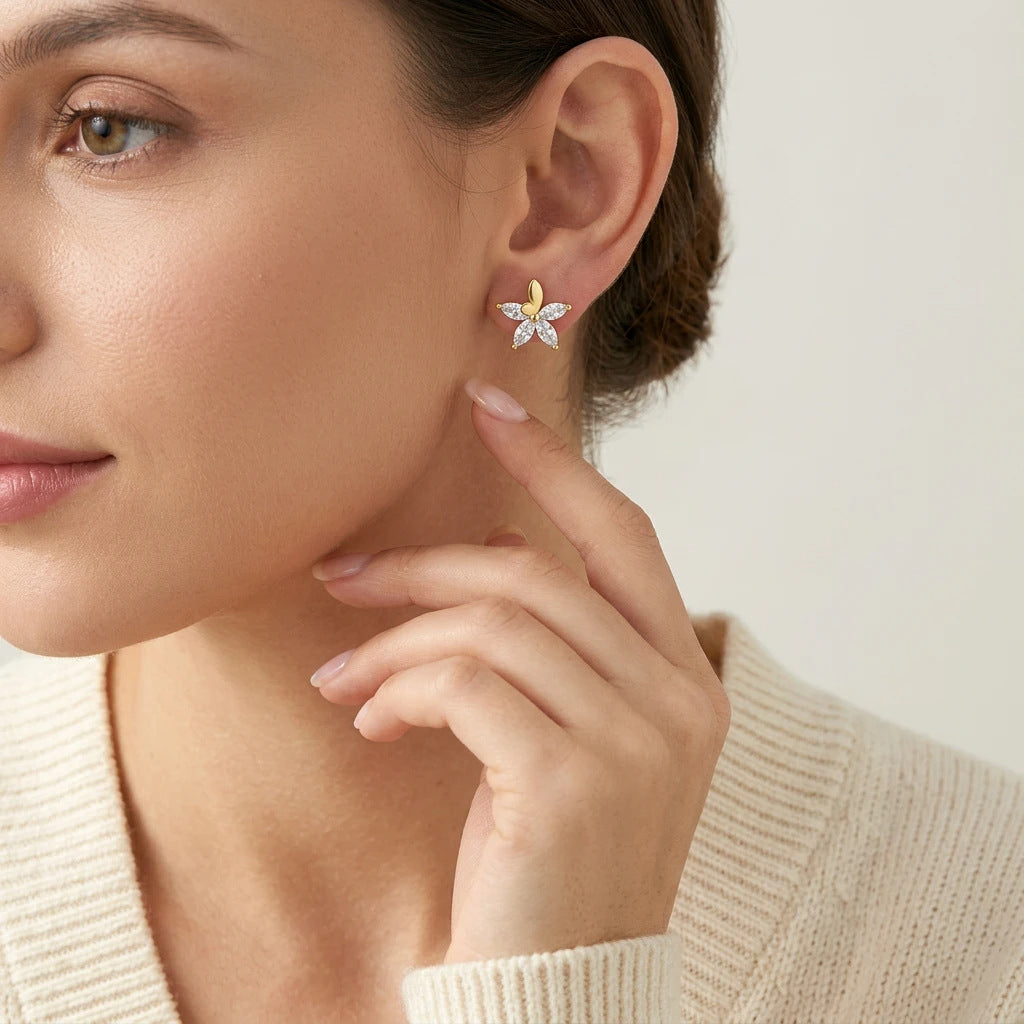 Editorial fashion lookbook portrait of a model styling timeless gold butterfly flower marquise moissanite stud earrings near her face.