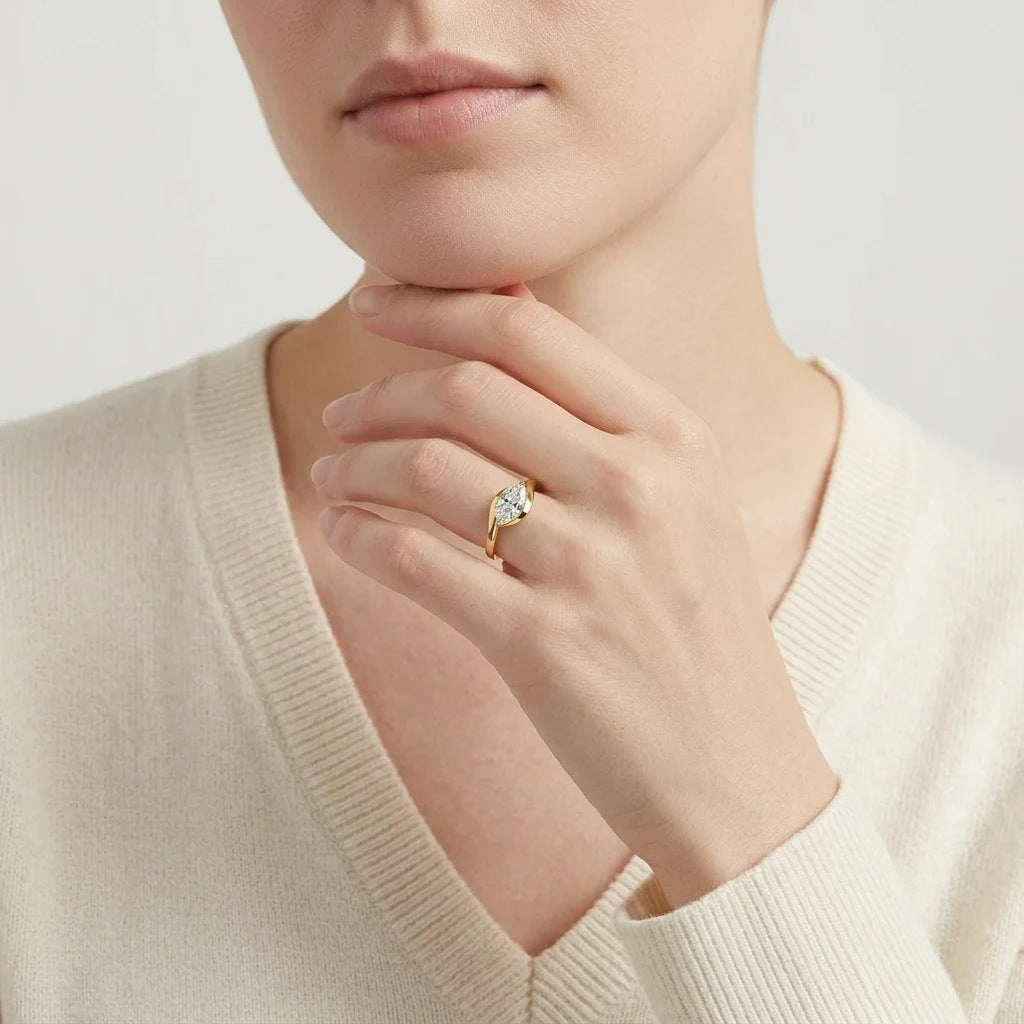 Editorial fashion lookbook portrait of a model styling an 18k gold east west marquise moissanite promise ring near her neck.