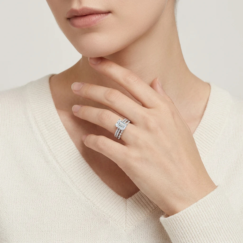 Editorial fashion lookbook portrait of a model styling a timeless romantic emerald cut moissanite 3 piece ring set near her chin.