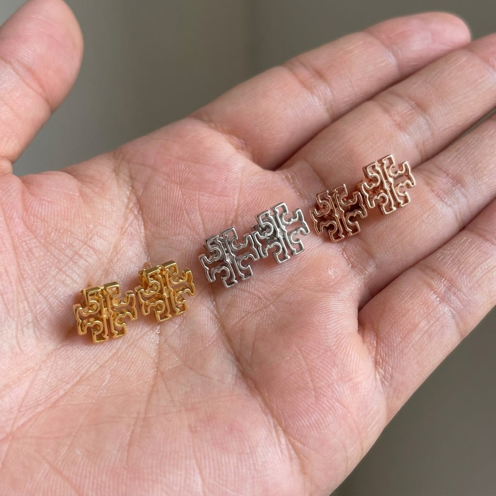 Hand-held size reference of Tory Burch Britten Logo Studs showing the actual scale on fingertips