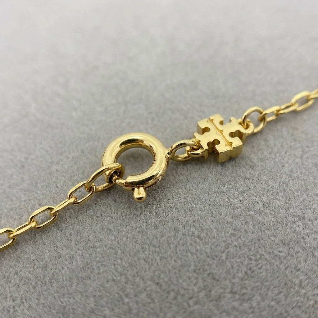 Detailed shot of the gold-tone lobster clasp and signature logo tag on the clover necklace
