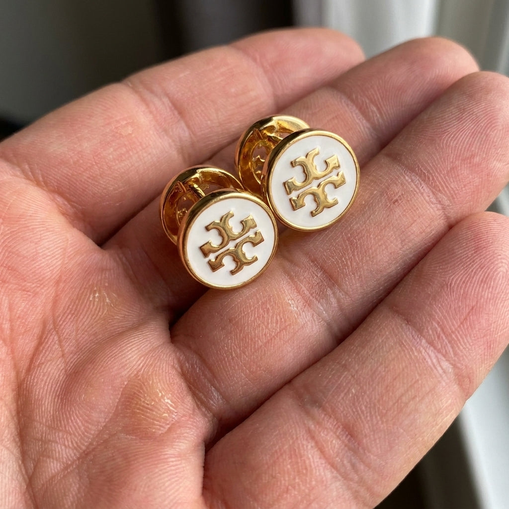 Hand-held size comparison of Tory Burch Icon Enamel Studs for accurate scale reference