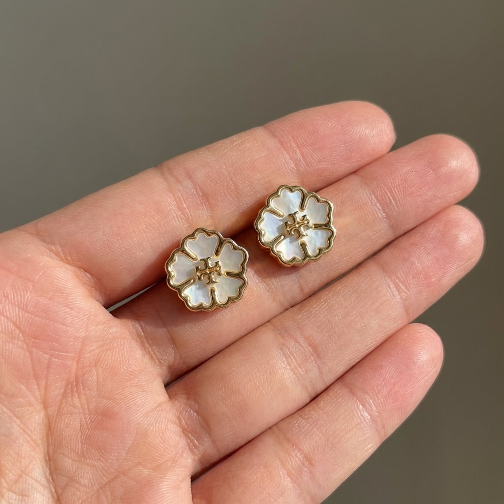 Flower-shaped earrings held between fingers against a neutral background