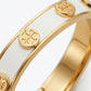 Macro detail of the polished gold edges and smooth white enamel finish on the Tory Burch cuff