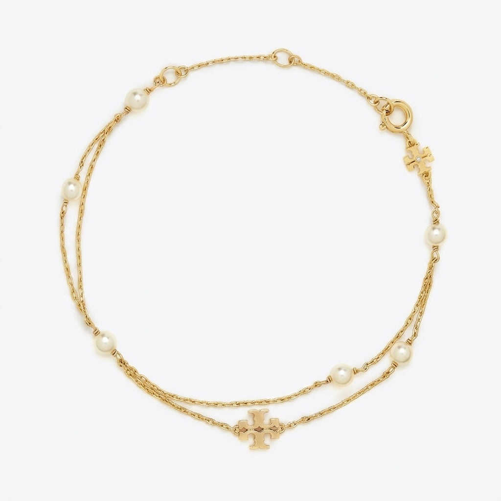 Flat lay view of Tory Burch gold moondance layered pearl bracelet featuring double T charm and glass pearls.