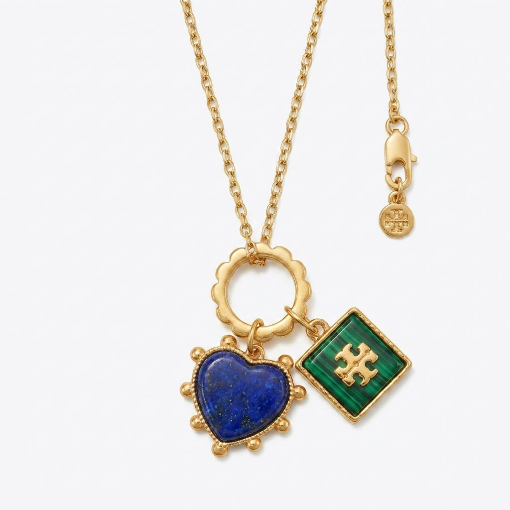 Gold necklace with heart-shaped blue pendant and green square pendant on a white background