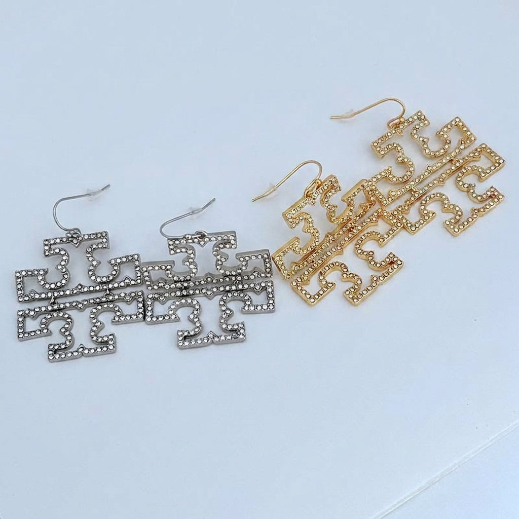 A real-life flat lay of the Tory Burch large Double T openwork pave earrings in both gold and silver color options.
