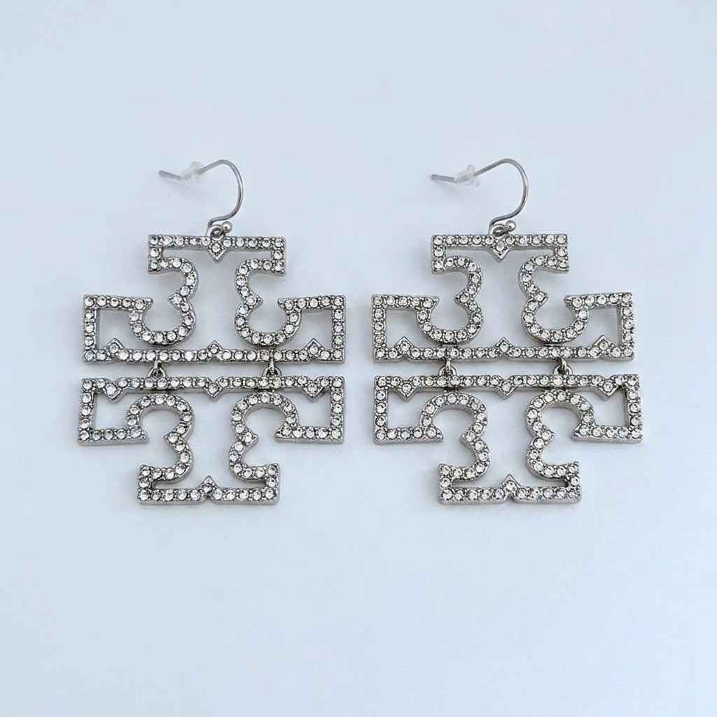 A close-up view of a model wearing the large Tory Burch Double T pave crystal statement earrings in gold to show scale and style.