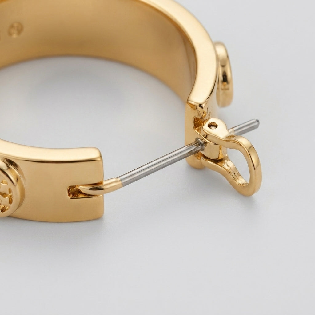 Close-up shot of the laser-cut Double T logo and polished gold texture on Miller Huggie Earrings