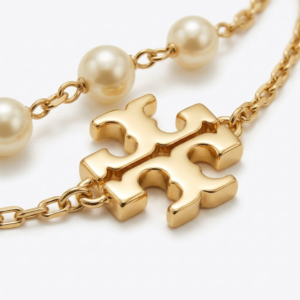 Studio macro close-up view highlighting gold-tone double T logo charm, delicate link chain, and luminous glass pearls.