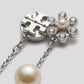Studio macro profile showing the back of double T logo post, crystalline flower detail, and silver chain pearl drop mechanism.