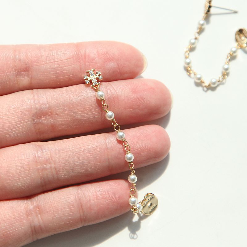 The Tory Burch Moondance Pearl and Chain Earrings held in hand to provide a real-life scale and size comparison