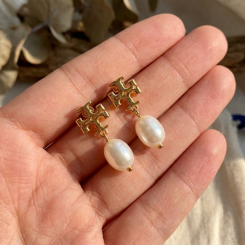 Hand-held size reference of Tory Burch Moondance Pearl Earrings to show dangle length and pearl scale